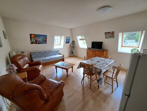 A living room with a sofa, a coffee table, a dining table with chairs, a television on a cabinet, and artwork on the walls. - Charm and Comfort** for a Family Vacation in La Bourboule (La Bourboule)