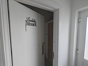 Um corredor com uma porta identificada como 'Lavanderia' e uma porta de madeira ao fundo.