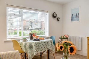 Ein Essbereich mit Tisch für zwei, einem Fenster mit Jalousien und einer Vase mit Sonnenblumen.