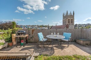 Eine Terrasse im Freien mit Grill, zwei Stühlen und einem Tisch.