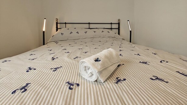 A single bed with a striped bedspread and a rolled towel. - 1 Bed in Brixham (oc-f45535) (Brixham)
