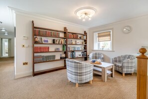 A library room with two plaid armchairs, a wooden table, and bookshelves filled with books. - 4 Bed in Wharton (oc-h45870) (Wharton)