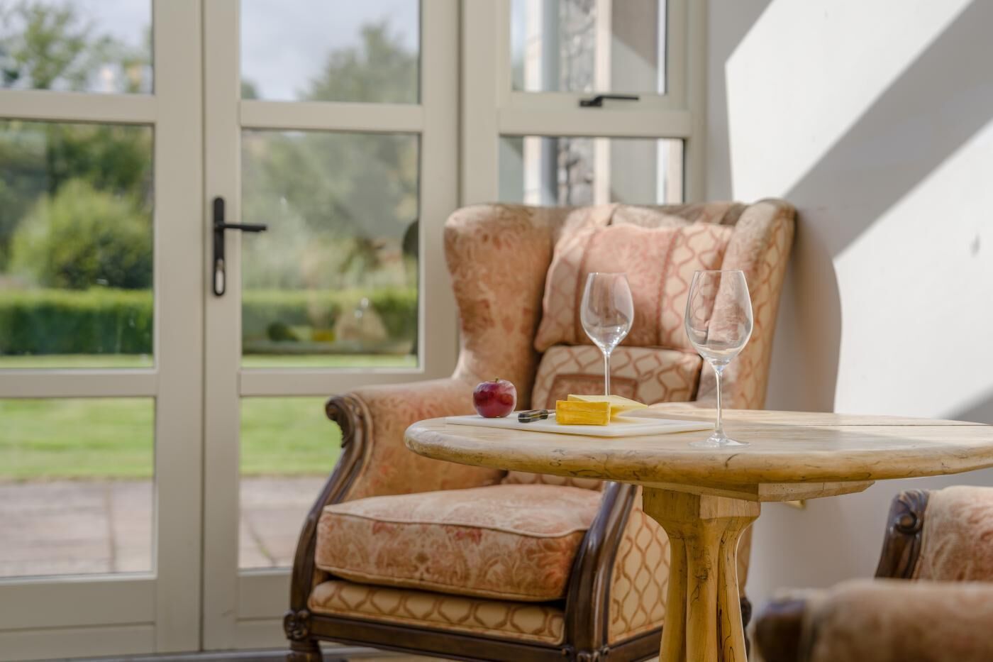 Une véranda avec un fauteuil rembourré, une petite table ronde et deux verres à vin.