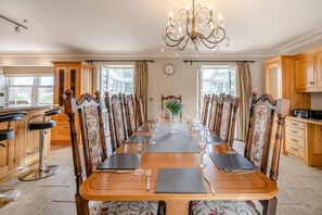 A dining room with a long table set for a meal, flanked by wooden chairs with floral upholstery, a chandelier, and a view through the windows. - 4 Bed in Wharton (oc-h45870) (Wharton)