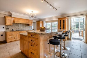 A kitchen with wooden cabinets, a granite countertop, a central island with stools, and a view through the glass doors. - 4 Bed in Wharton (oc-h45870) (Wharton)