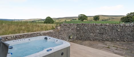 A hot tub on a wooden deck with a stone wall and a view of rolling hills.