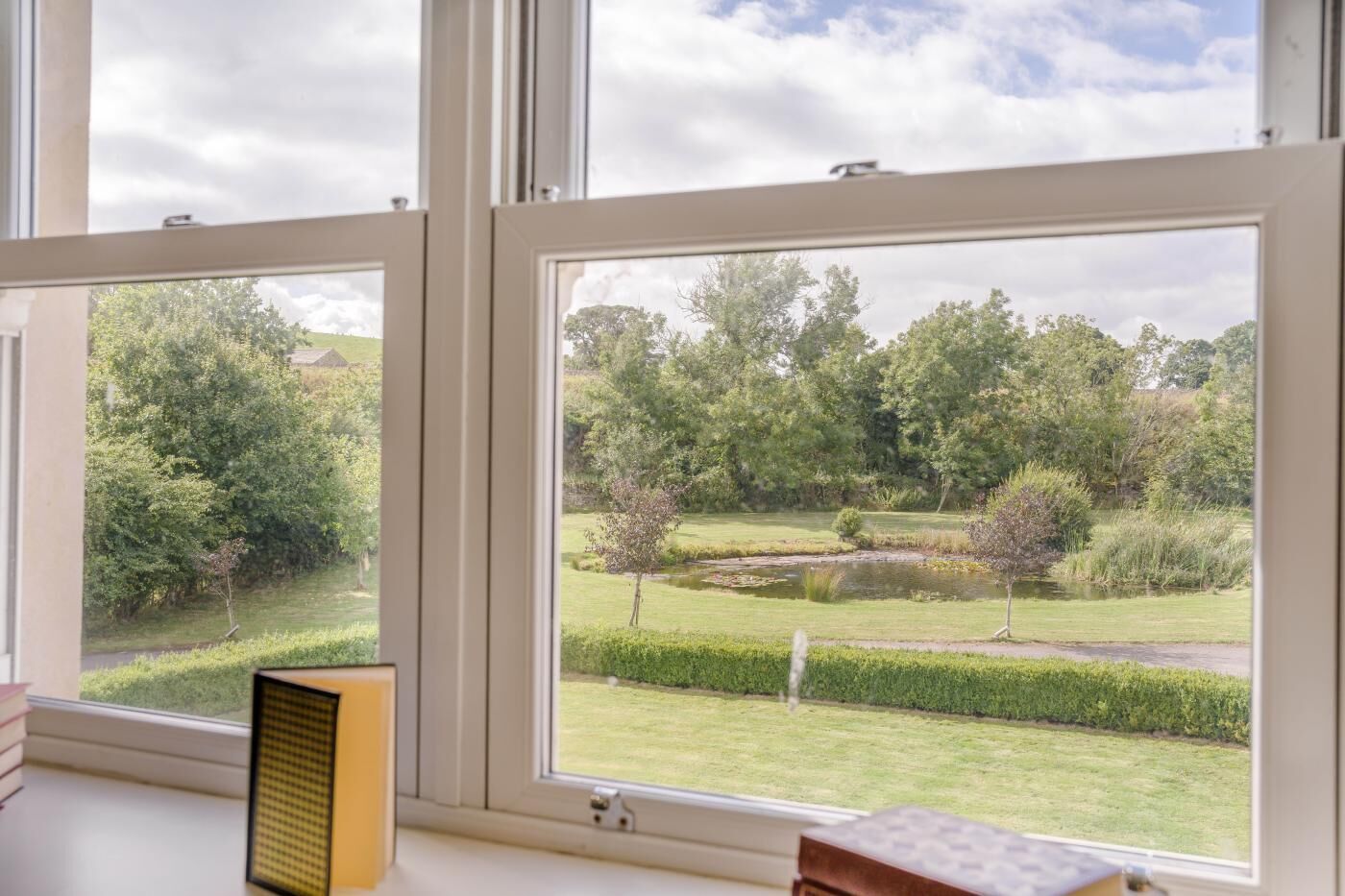 A room with large windows overlooking a garden with a pond and trees.