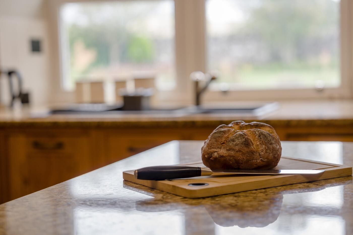 A loaf of bread on a wooden cutting board on a kitchen counter.