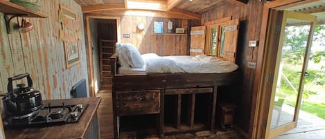 A rustic cabin interior with a bunk bed, a small kitchenette with a gas stove, and a view of the outdoors through a glass door.