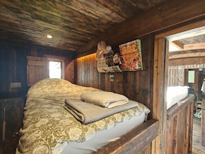 A rustic wooden room with a bed, a window, and a wall-mounted shelf with books and a teddy bear. - 2 Bed in Earsdon (oc-s45692) (Earsdon)