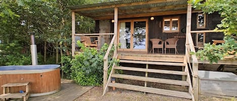 A wooden cabin with a porch, outdoor seating, and a hot tub.
