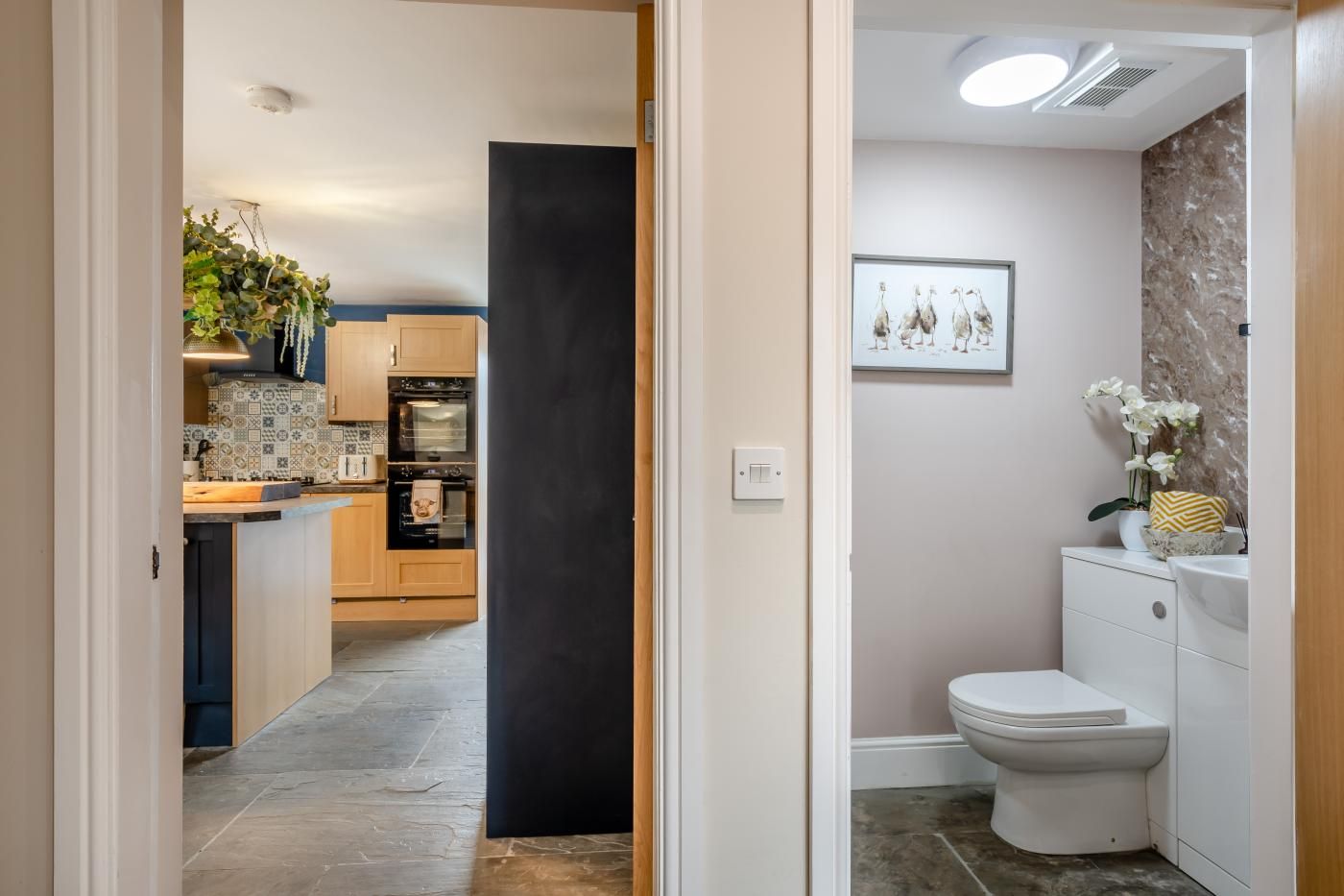 Eine moderne Küche mit Holzschränken und einer Fliesenküchenwand, die zu einem Badezimmer mit Toilette und Waschbecken führt.