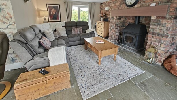 A living room with a sofa, a coffee table, a fireplace, and a clock on the wall. - 3 Bed in Grizebeck (oc-b45345) (Kirkby Ireleth)