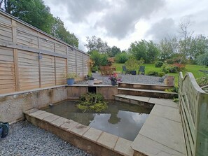 Ein Garten mit Teich, Holzzaun und Sitzgelegenheit im Freien.