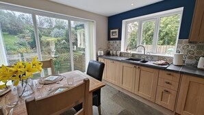 A modern kitchen with a dining area, large windows, and a view of the garden. - 3 Bed in Grizebeck (oc-b45345) (Kirkby Ireleth)