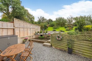 A patio with a table and chairs, a small pond, and a garden with various plants and a wooden fence. - 3 Bed in Grizebeck (oc-b45345) (Kirkby Ireleth)