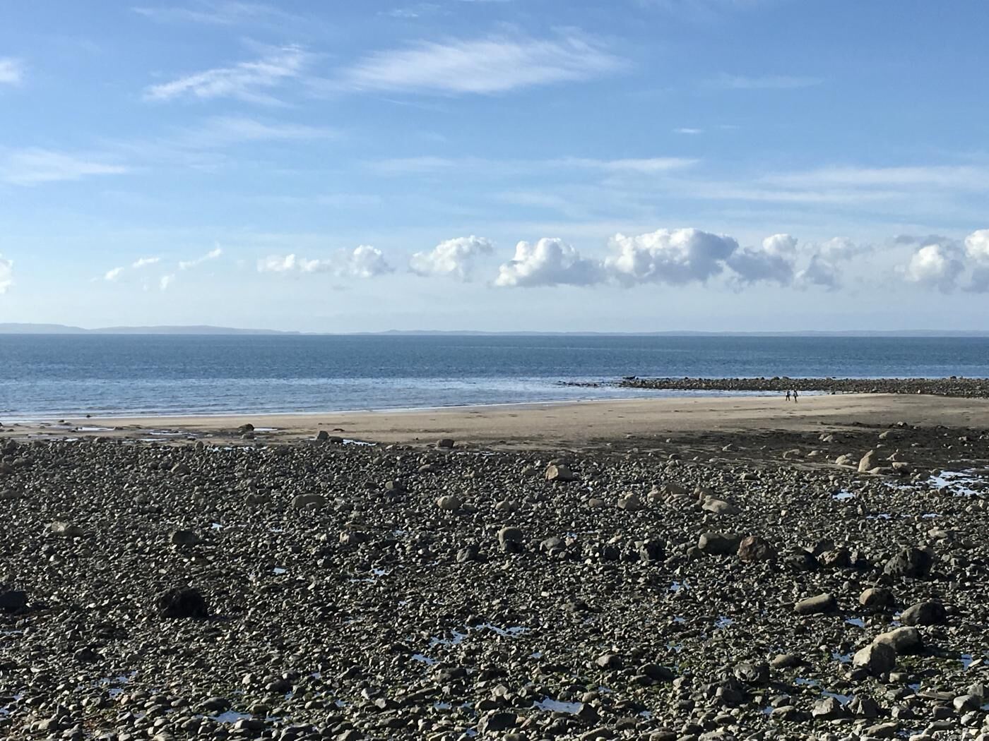 Une plage de galets, avec un ciel dégagé et une mer calme.