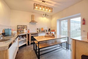 A modern kitchen with a central island, stainless steel appliances, and a large window providing natural light. - 3 Bed in Port William (oc-s45456) (Port William)