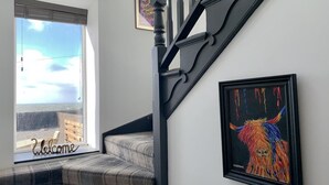 Eine Treppe mit schwarzer Geländer, ein gerahmtes Bild an der Wand und ein Fenster mit einem 'Welcome'-Schild.