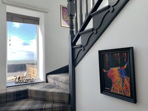 A staircase with a black handrail, a framed painting on the wall, and a window with a 'Welcome' sign. - 3 Bed in Port William (oc-s45456) (Port William)