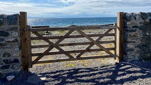 Ein hölzernes Tor führt zu einem felsigen Strand mit Blick auf das Meer.
