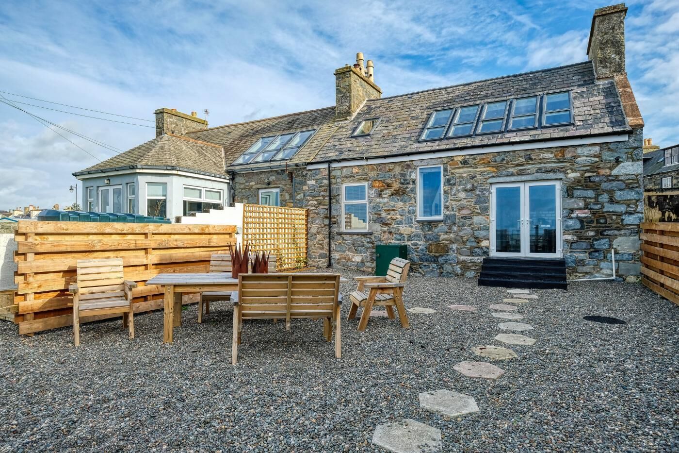 A stone house with a gravel patio, wooden furniture, and a clear sky.