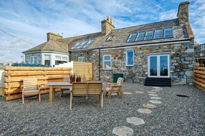 A stone house with a gravel patio, wooden furniture, and a clear sky. - 3 Bed in Port William (oc-s45456) (Port William)