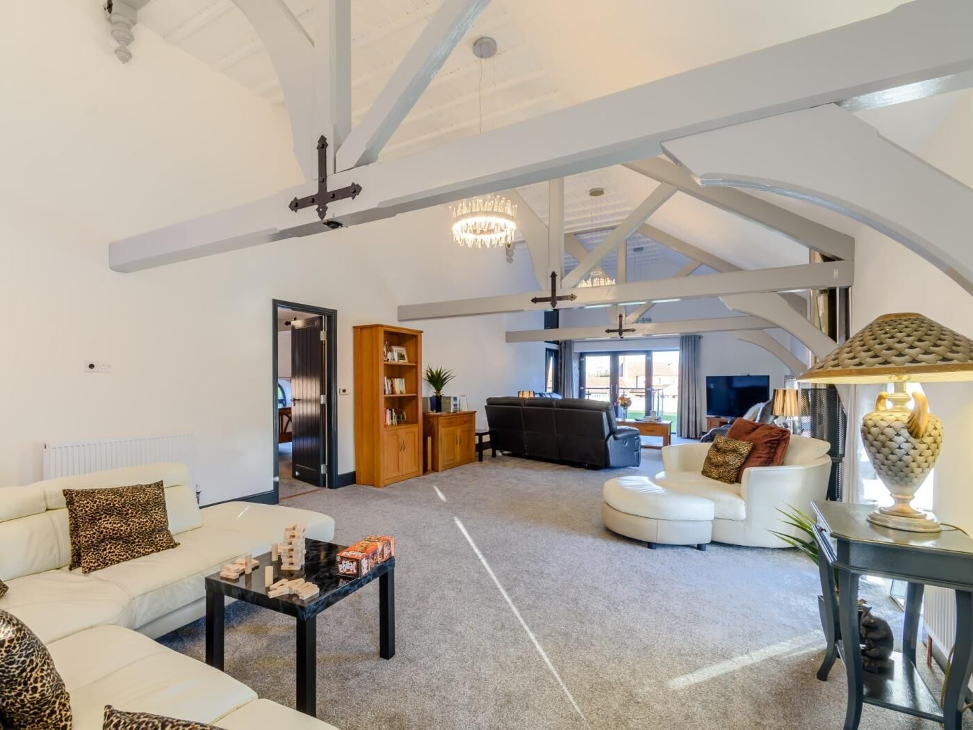 A spacious living room with a high ceiling, a chandelier, and a fireplace. There is a sofa set, a coffee table, and a television.
