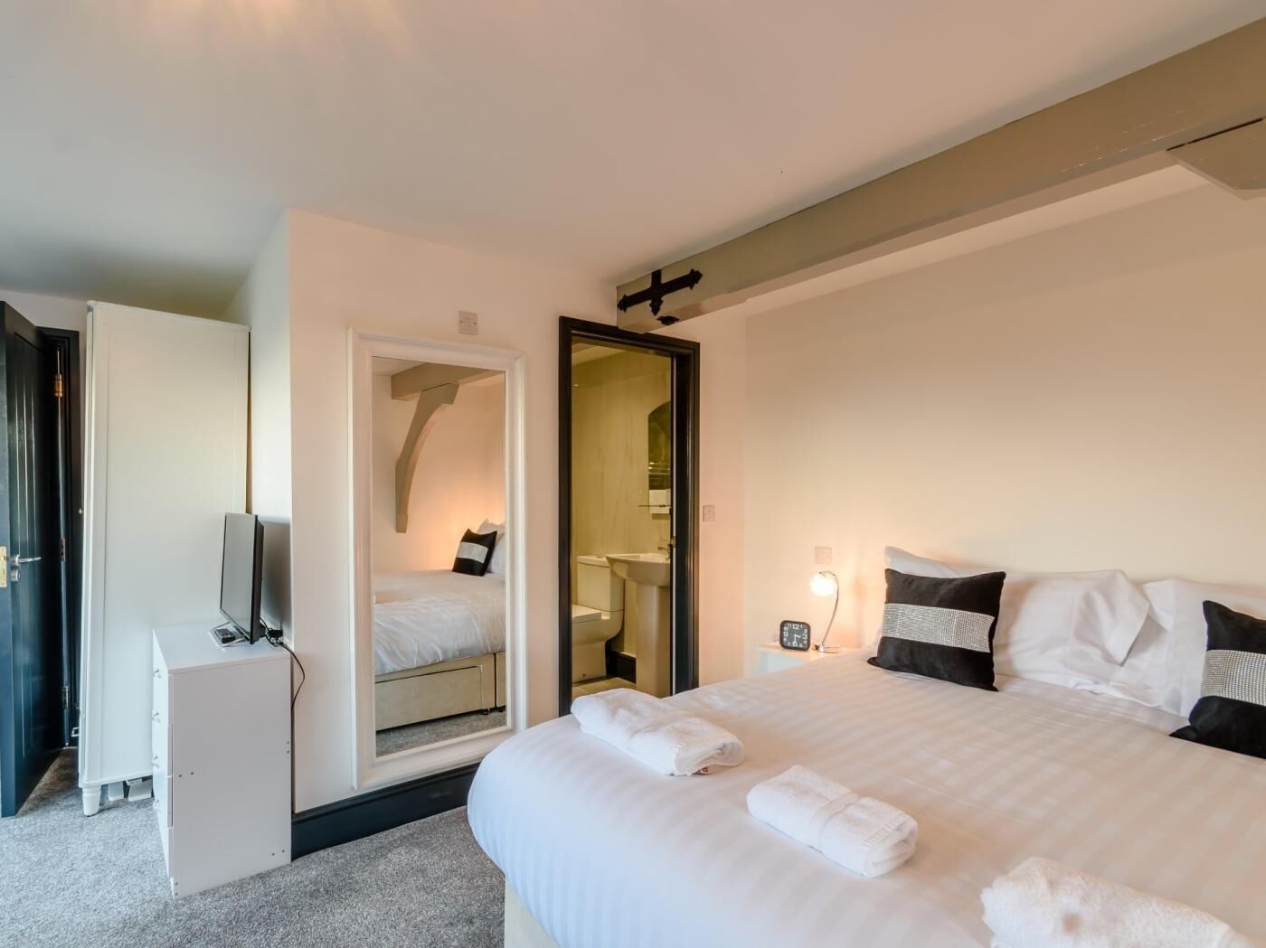 A hotel room with a bed, a TV, a mirror, and a bathroom visible through an open door.