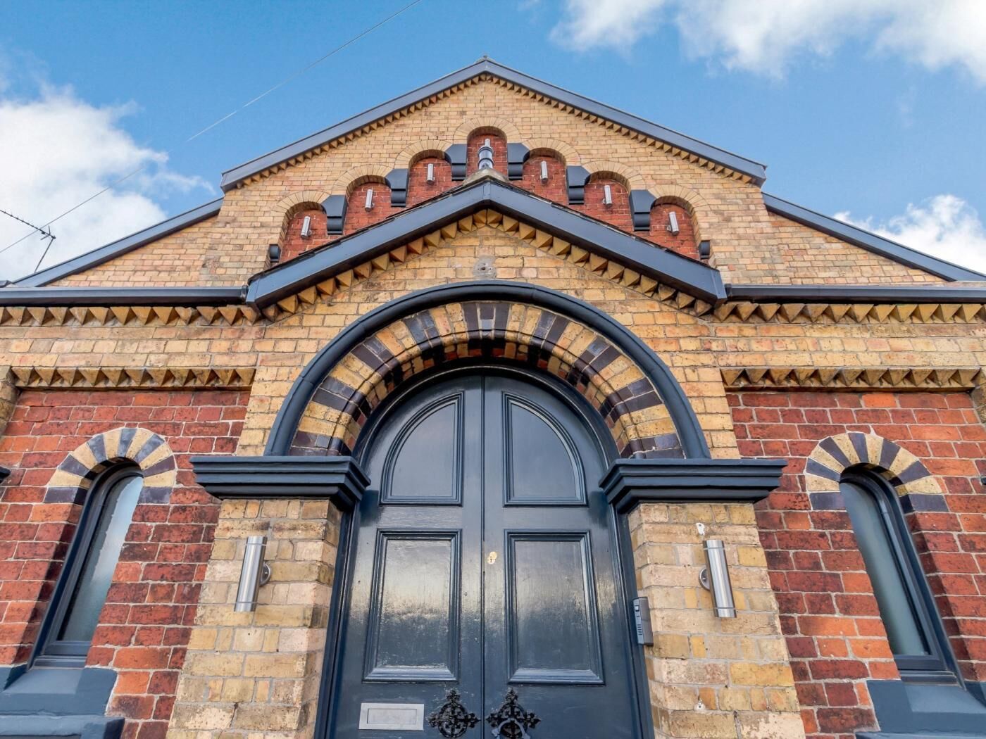 Ein Gebäude mit einer auffälligen schwarzen Tür, bogenförmigen Fenstern und einer Ziegel-Fassade.