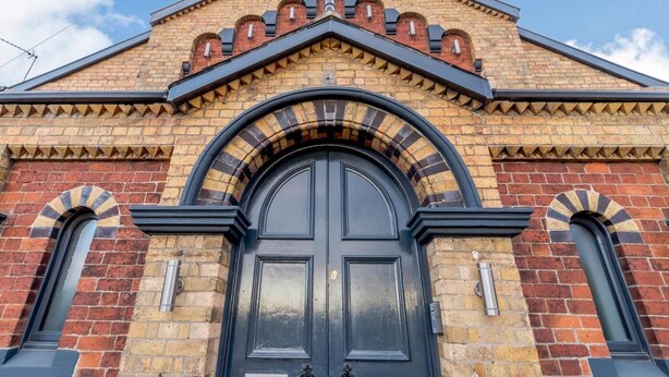 Ein Gebäude mit einer auffälligen schwarzen Tür, bogenförmigen Fenstern und einer Ziegel-Fassade.