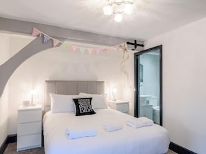 A bedroom with a bed, nightstands, a clock, a pillow, a towel, a hanging light fixture, and a bathroom visible through an open door. - 5 Bed in Driffield (oc-80371) (Burton Fleming)