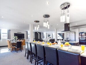 A modern kitchen with stainless steel appliances, a dining area with a long table and chairs, and a living space with a large window. - 5 Bed in Driffield (oc-80371) (Burton Fleming)