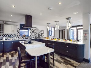 A modern kitchen with a central island, dark cabinetry, and a checkered backsplash. - 5 Bed in Driffield (oc-80371) (Burton Fleming)
