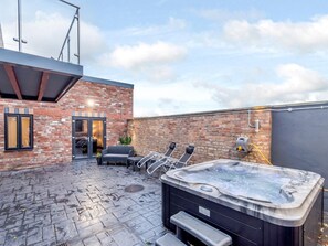 A rooftop patio with a hot tub, seating area, and a brick building.