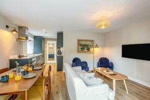 Ein modernes Wohnzimmer mit einer Couch, Sesseln, einem Esstisch mit Frühstücksgebäck und -speisen, einem Fernseher und einem Gemälde an der Wand.