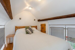 A bedroom with a large bed, a wooden headboard, a small bedside table, and a door with a metal gate. - 1 Bed in Ambleside (oc-a45864) (Ambleside)