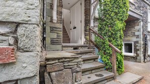 A stone staircase leading to a white door, with a wooden handrail and a green plant wall. - 1 Bed in Ambleside (oc-a45864) (Ambleside)