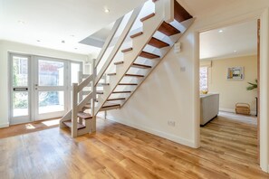 A modern interior with a wooden staircase, a large glass door leading outside, and a view of a cityscape. - 4 Bed in Beccles (oc-b45848) (Beccles)