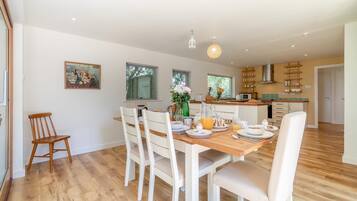 A dining area with a wooden table set for breakfast, white chairs, and a kitchen in the background.