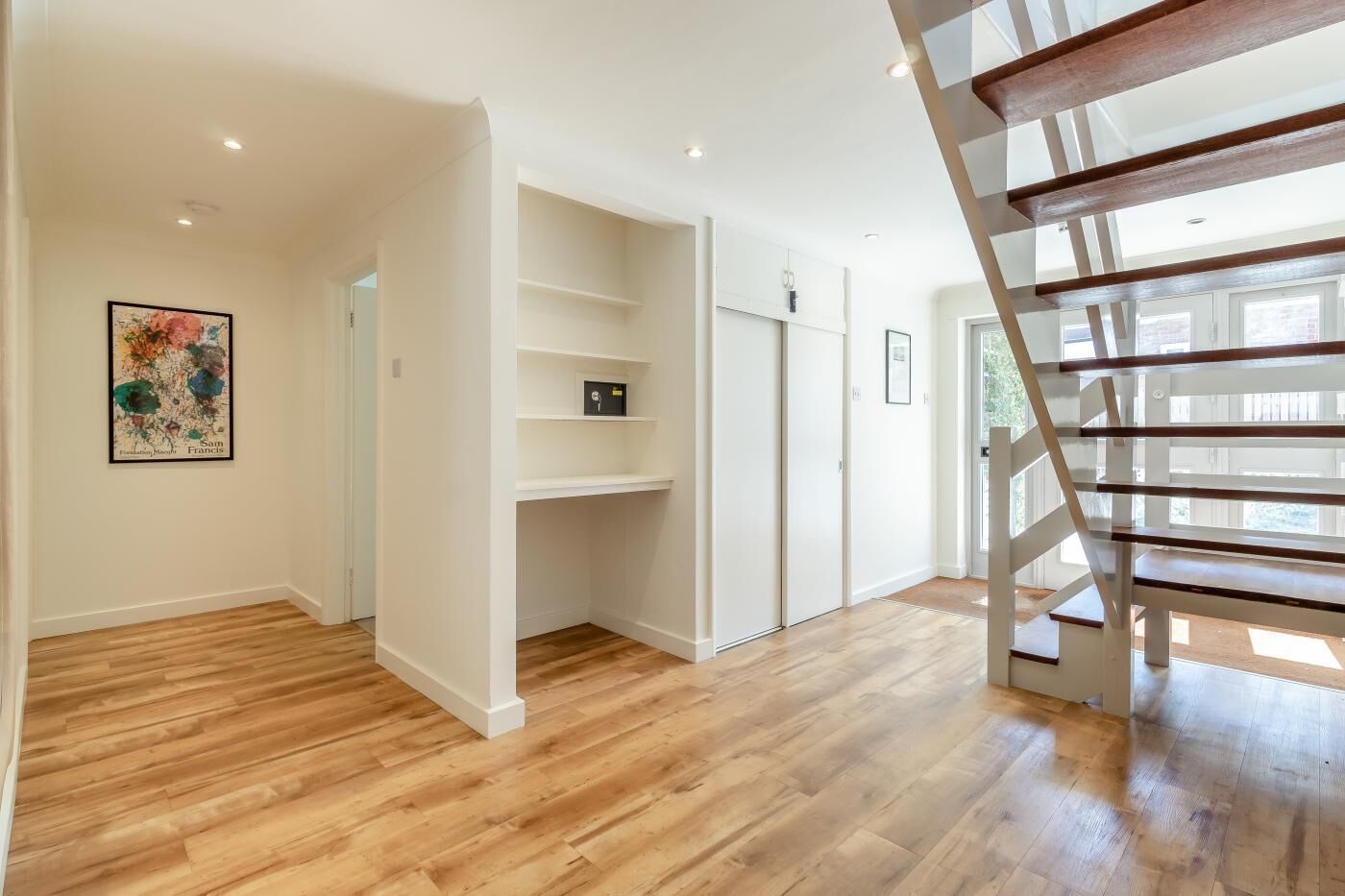 A spacious room with wooden flooring, a white staircase, and built-in shelving.