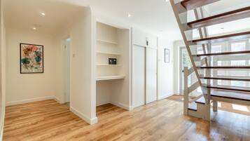 A spacious room with wooden flooring, a white staircase, and built-in shelving.