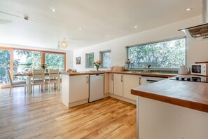 Una cocina moderna con suelo de madera, armarios blancos y un amplio ventanal con vistas al exterior.