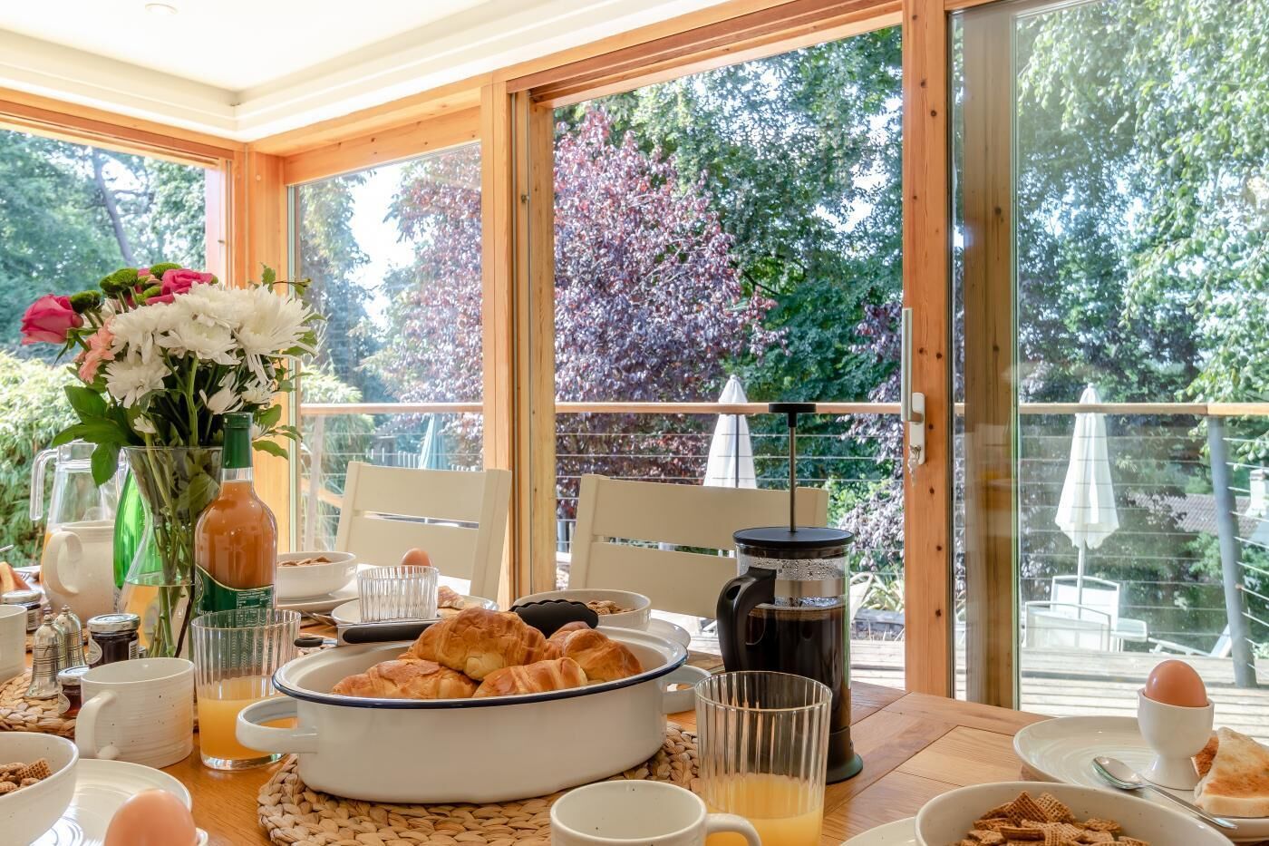 Une table de petit-déjeuner avec des croissants, du café et un vase de fleurs.