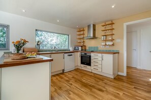 A modern kitchen with a wooden countertop, a dishwasher, an oven, and a window with a view of trees. - 4 Bed in Beccles (oc-b45848) (Beccles)