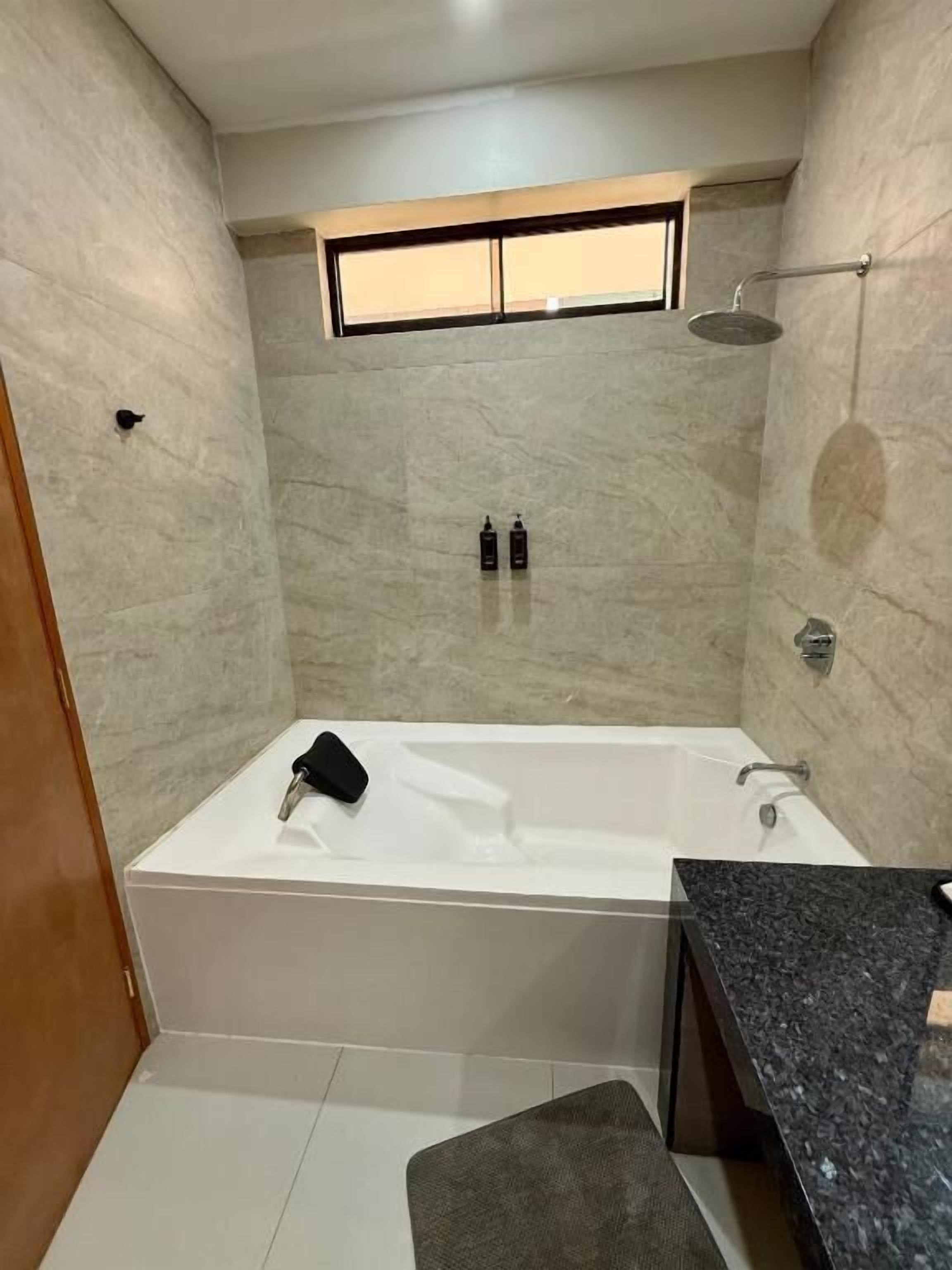 A bathroom with a bathtub, a shower, and a window. There are toiletries on the wall.
