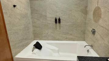 A bathroom with a bathtub, a shower, and a window. There are toiletries on the wall.