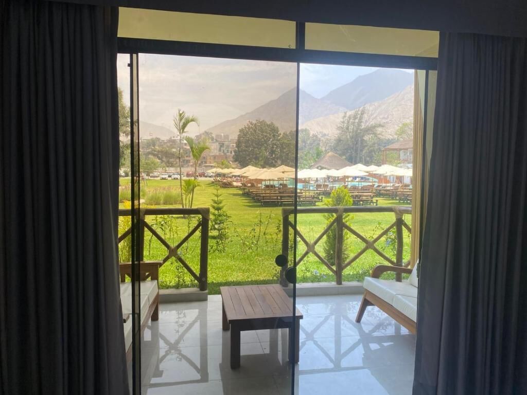 Una habitación con vista a un área verde y montañas. Hay una mesa de madera y un banco.