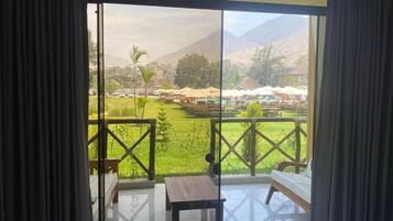 Una habitación con vista a un área verde y montañas. Hay una mesa de madera y un banco.