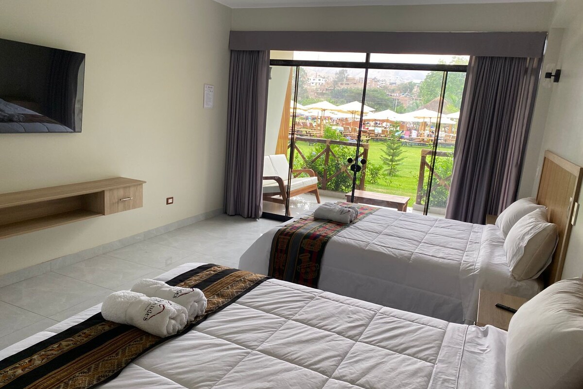 A hotel room with two beds, a TV mounted on the wall, and a balcony with a view of the city.